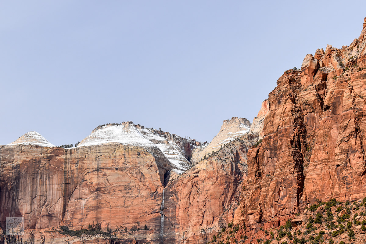 Snow-dusted red sandstone cliffs beneath a pale blue sky, photographed by Yusuf